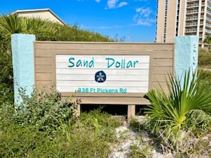 Letrero de 'Sand Dollar' en 336 Ft Pickens Rd, rodeado de follaje y cielo despejado.