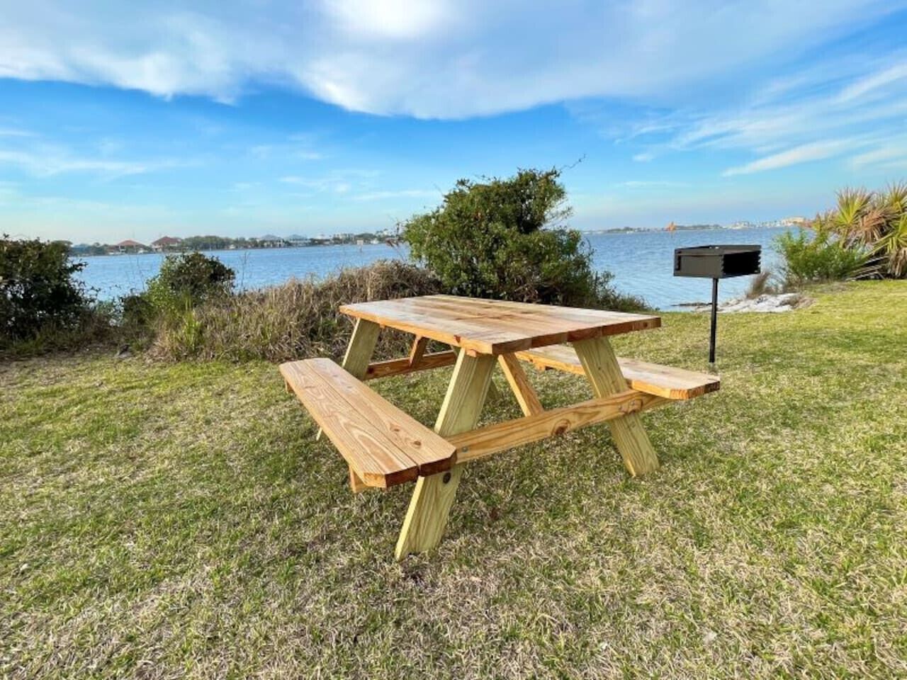 A wooden picnic table with benches in a grassy area near a body of water.