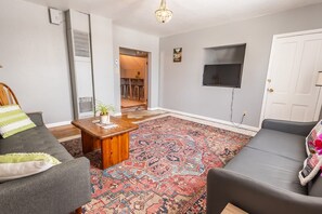 Un salon avec un canapé gris, une table basse en bois et un tapis à motifs.