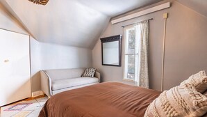 Een slaapkamer met een groot bed, een raam met gordijnen, een bank en een spiegel aan de muur.