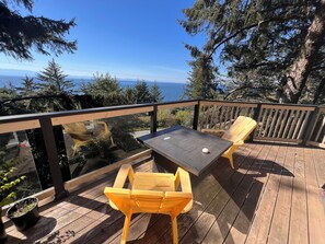 Une terrasse en bois avec une table et deux chaises jaunes, donnant sur une étendue d’eau et des arbres.