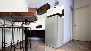 A compact kitchen with a white refrigerator, a wooden table with metal chairs, and a microwave on the counter.
