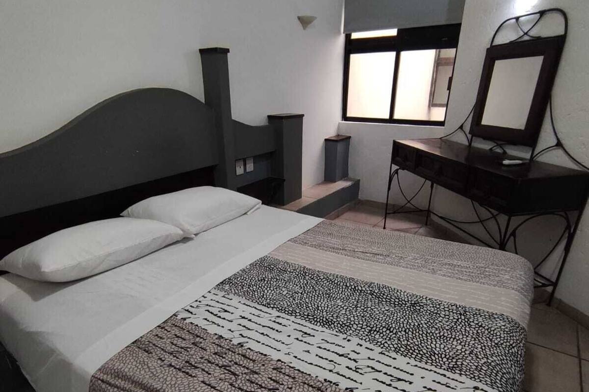 A bedroom with a bed, a desk, a chair, an air conditioner, and a window.