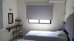 Ein Zimmer mit zwei Betten, einem Schreibtisch, einem Stuhl, einem Fenster mit Jalousien und einer Klimaanlage.