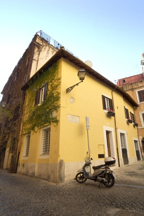A yellow building with a cobblestone street, a parked scooter, and a street lamp.