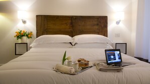 Un lit bien fait, avec un ordinateur portable, un plateau contenant des aliments pour le petit-déjeuner et un vase rempli de fleurs.