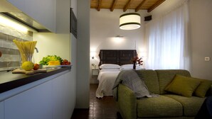 Un espace de vie compact comprenant un coin cuisine, un canapé vert, un lit et une grande fenêtre.