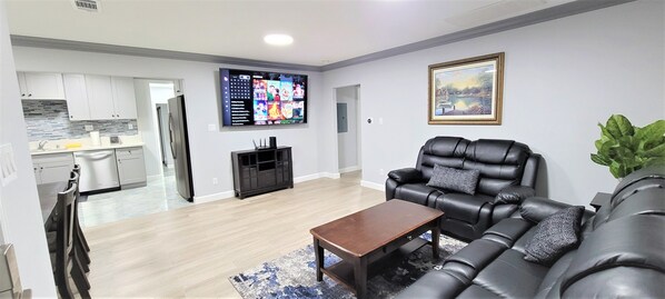Uma sala de estar moderna com um sofá de couro preto, uma mesa de centro de madeira e uma grande TV de tela plana fixada na parede.