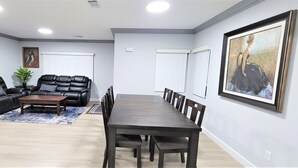 Een ruime woonkamer met een donker houten eettafel, leren banken en een blauw vloerkleed.