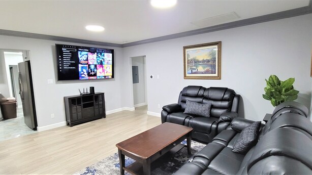 Een moderne woonkamer met een zwarte leren bank, een houten salontafel en een flatscreen televisie die aan de muur is bevestigd.