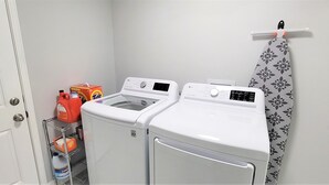Een wasruimte met twee witte wasmachines, een plank met wasmiddelflessen, en een gordijn met een patroon.
