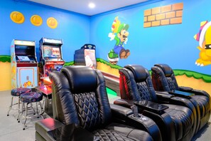 A room with gaming machines, reclining chairs, and a Mario-themed mural. - Epic 9BR Game House - Arcade, PS5, Pool & Hot Tub (Davenport)