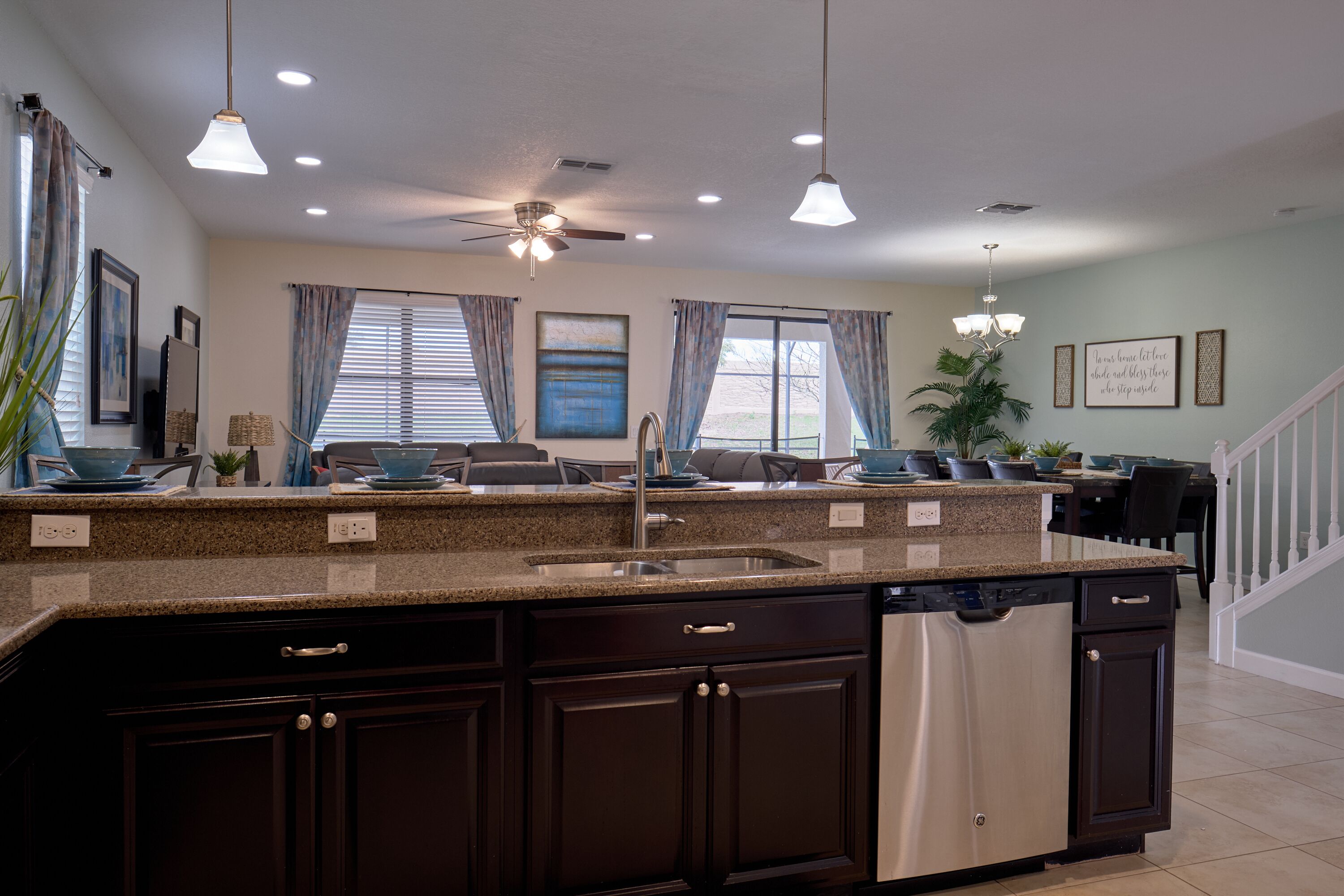 A modern kitchen with granite countertops, a built-in dishwasher, dark cabinetry, and pendant lighting.