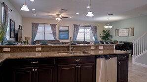 A modern kitchen with dark cabinetry, a granite countertop, a built-in dishwasher, and pendant lighting. - Epic 9BR Game House - Arcade, PS5, Pool & Hot Tub (Davenport)