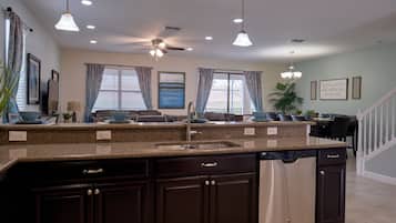 A modern kitchen with granite countertops, a built-in dishwasher, dark cabinetry, and pendant lighting.