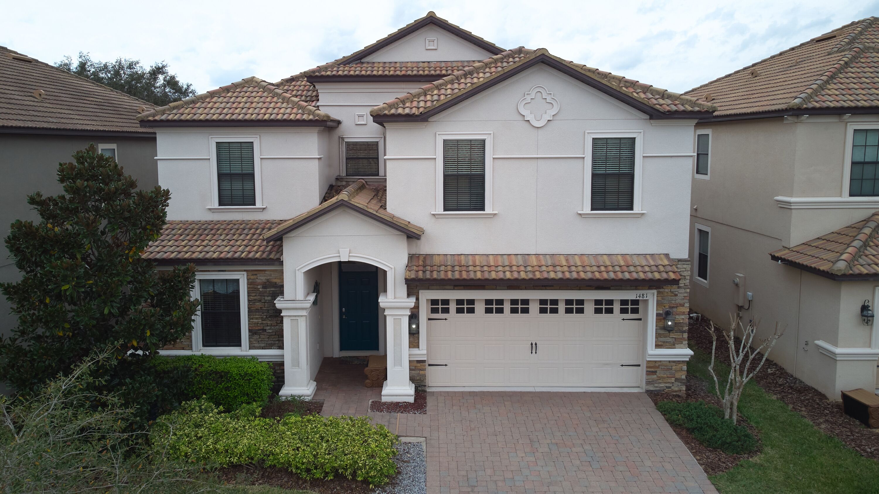 A two-story house with a garage, a front entrance with a small porch, and a tiled roof.