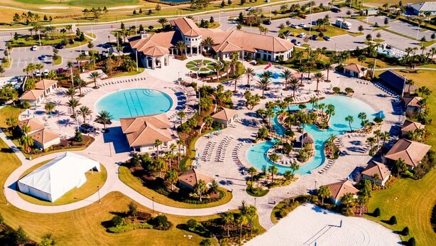 An aerial view of a resort with multiple swimming pools, palm trees, and a large white tent. - Epic 9BR Game House - Arcade, PS5, Pool & Hot Tub (Davenport)