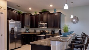 A modern kitchen with dark wood cabinets, stainless steel appliances, a granite countertop, and a breakfast bar with chairs. - Epic 9BR Game House - Arcade, PS5, Pool & Hot Tub (Davenport)