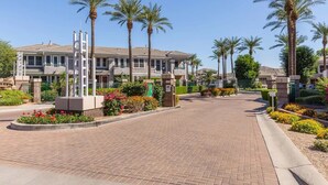 Zona residencial con entrada pavimentada, palmeras y urbanización privada.