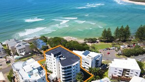 A coastal hotel with multiple floors, a rooftop pool, and a view of the ocean.