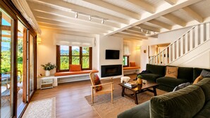 Ein geräumiges Wohnzimmer mit Kamin, einer Sofagarnitur, einem Fernseher und einer Treppe.