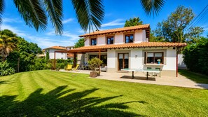 A two-story house with a patio, a lawn, and a garden.