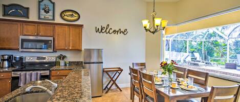 A kitchen with granite countertops, stainless steel appliances, and a dining area with wooden chairs and a table set for two.