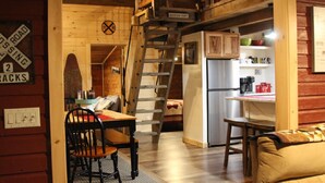 Een rustiek houten huisje met een eethoek, keuken en een slaapkamer op een entresol.