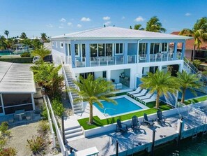 A modern two-story house with a swimming pool, outdoor seating, and palm trees.