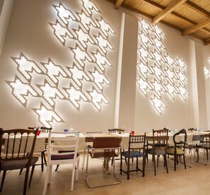 A restaurant interior with modern decor, wooden ceiling beams, and patterned wall lighting. Tables are set with chairs, and a bar area is visible. - Family house - 2 verandas - outdoor kitchen - exercise bike - 6 km from beaches (Carovigno)