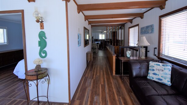 A hallway with wooden flooring, a brown leather sofa with a blue fish-patterned pillow, and a green seahorse decoration on the wall.