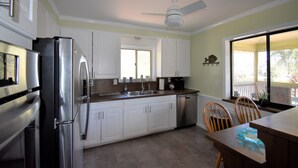 A kitchen with white cabinets, stainless steel appliances, a dishwasher, and a dining area with wooden chairs.