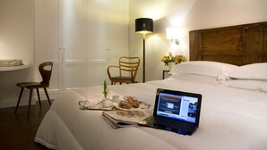 Et hotelværelse med seng, en bærbar computer, stol, lampe og et lille bord med blomstervase.