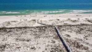 Une plage avec un sentier sablonneux menant à l’eau, un ciel dégagé et l’océan en arrière-plan.