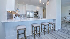 Une cuisine moderne avec des meubles blancs, des appareils en acier inoxydable et un coin bar équipé de tabourets.