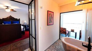 Ein Hotelzimmer mit Bett, einem Badezimmer mit Badewanne, einem Balkon mit Blick und einer Tür zu einem weiteren Raum.