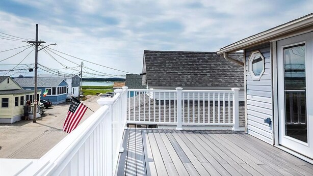 A wooden deck with a white railing, overlooking a residential area with houses and a body of water. - Beach Condo with a view! 3-bedroom with balcony porch! (Hampton)