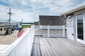 A wooden deck with a white railing, overlooking a residential area with houses and a body of water. - Beach Condo with a view! 3-bedroom with balcony porch! (Hampton)
