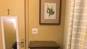 Une pièce avec une porte, un miroir, une commode, un tableau encadré et un rideau.