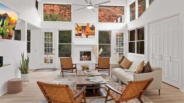 A spacious living room with a fireplace, large windows, and a ceiling fan.