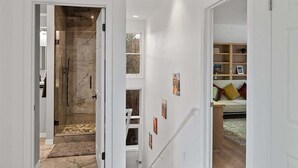 A modern interior with a glass shower, a staircase, and a living area with a sofa and bookshelves.
