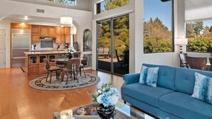 A modern kitchen with a dining area, a blue sofa, and large windows overlooking a garden. - Lux 2-King Suite Luxury Townhome! Pool + Hot Tub! (Sedona)