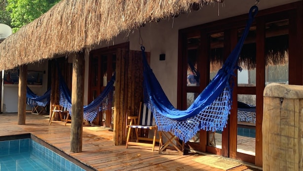A poolside area with hammocks and wooden chairs, a thatched roof, and a pool.