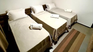 A room with three single beds, a wooden ceiling, and a wall-mounted air conditioner.