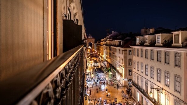 Ein belebter Straßenansicht bei Nacht, mit historischen Gebäuden und einem markanten Glockenturm.