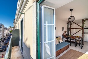 A balcony with a view of a busy street, a sliding glass door, a wooden bench, a dining table with chairs, and a kitchen area.