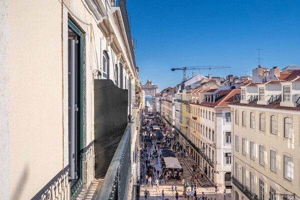 A crowded street with buildings on both sides, a clear sky, and a construction crane in the distance.