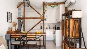 Eine kleine Küche mit weißen Schränken, einem Holztisch mit Stühlen, einer Pendelleuchte und einem eingebauten Bücherregal mit Lampe.