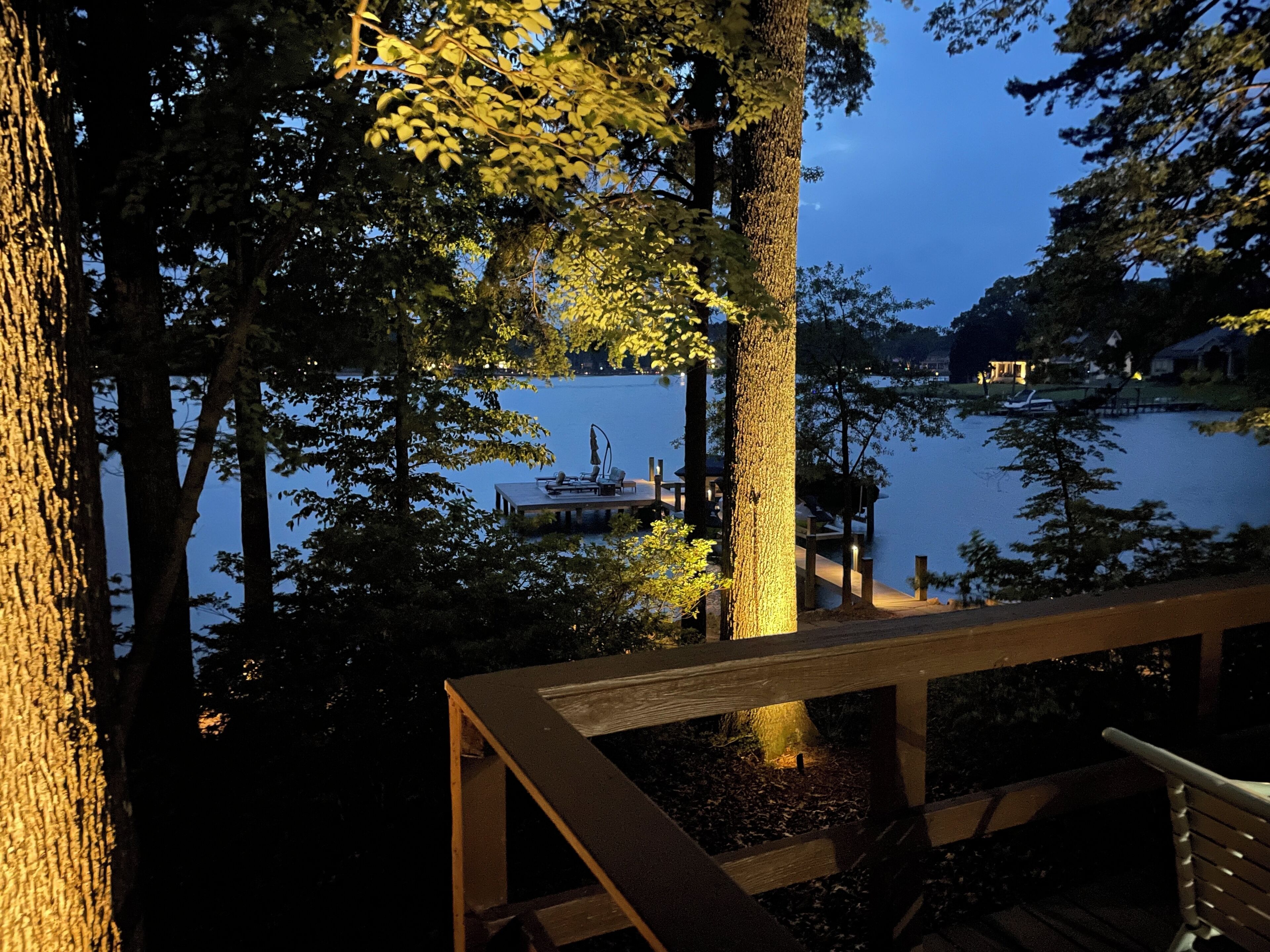 A wooden deck overlooking a calm lake with docked boats, surrounded by trees.