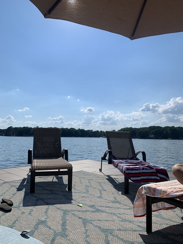 Relax in a serene lakeside setting with a shaded patio featuring two lounge chairs and a calm view.